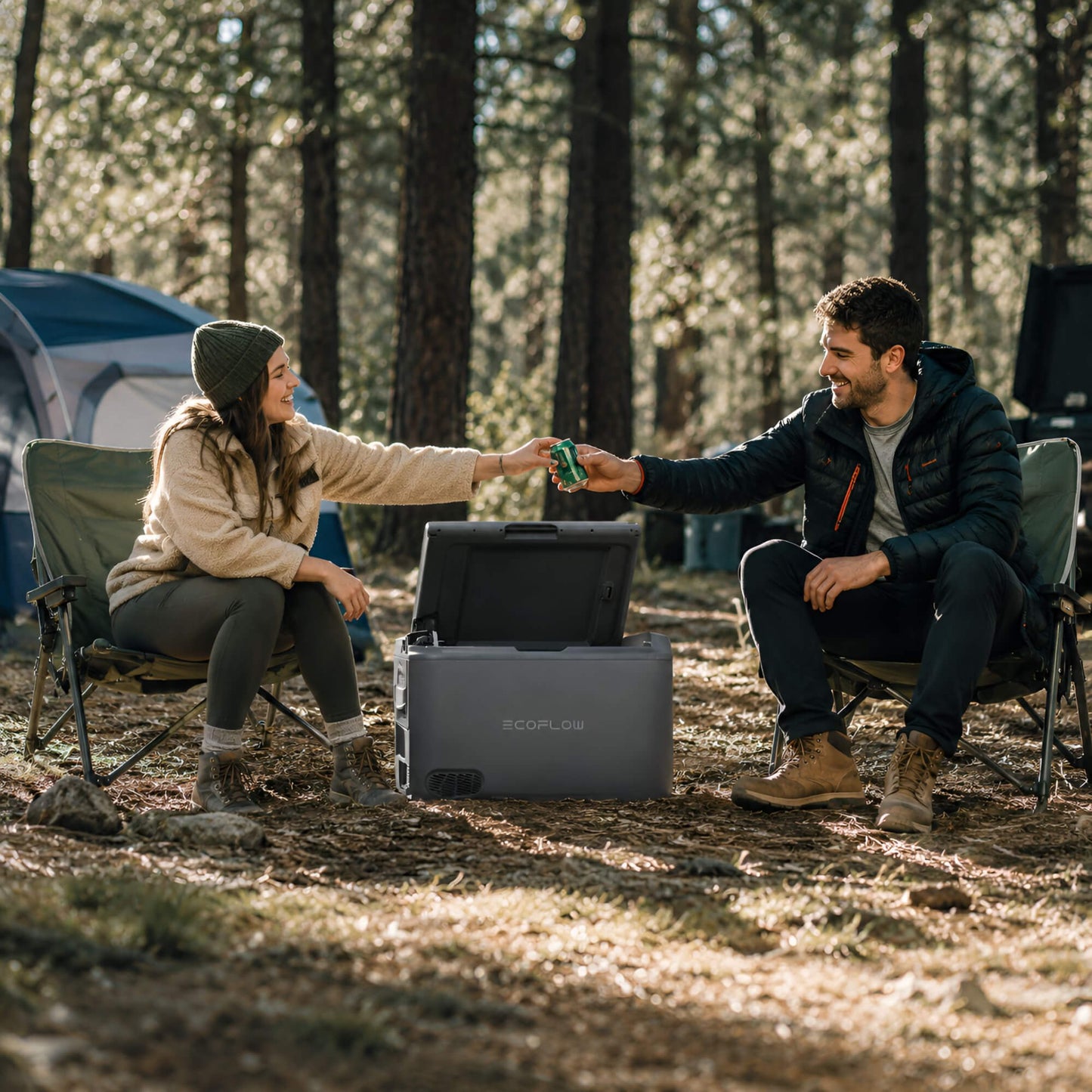 Een man en vrouw op een camping in het bos die een koud drankje pakken uit de EcoFlow Glacier draagbare koelbox.