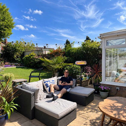 Zwarte Herschel MIAMI 2000 W infrarood terrasverwarmer op zwarte standaard naast een loungeset in de tuin