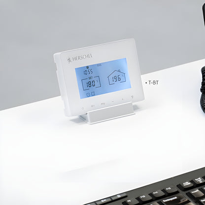 Witte Herschel T-BT thermostaat op batterijen, geplaatst op een bureau met zichtbaar display voor infraroodverwarming