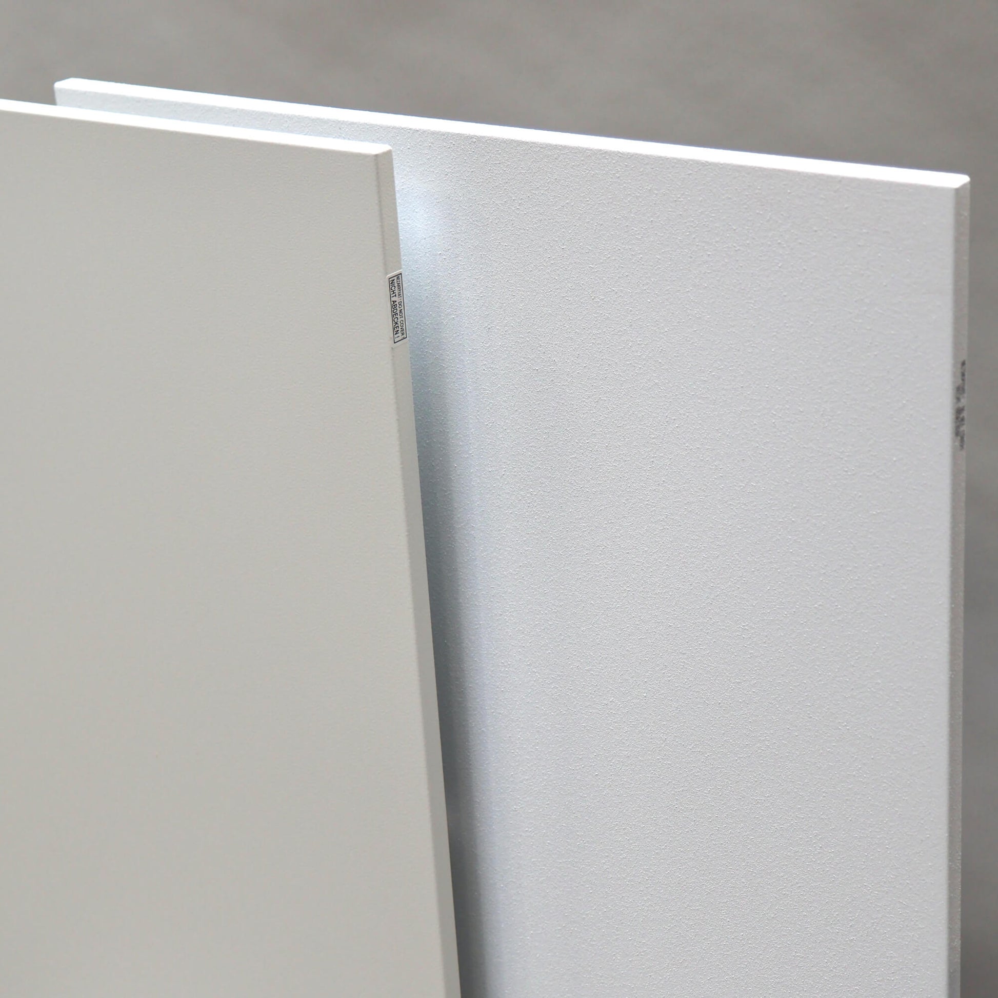 Twee witte Nova infrarood verwarmingspanelen naast elkaar met verschil tussen glad oppervlak en fijne structuur