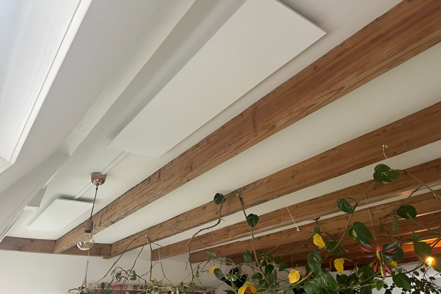 2 witte Nova infrarood verwarmingspanelen gemonteerd aan het plafond in een woonruimte met houten balken