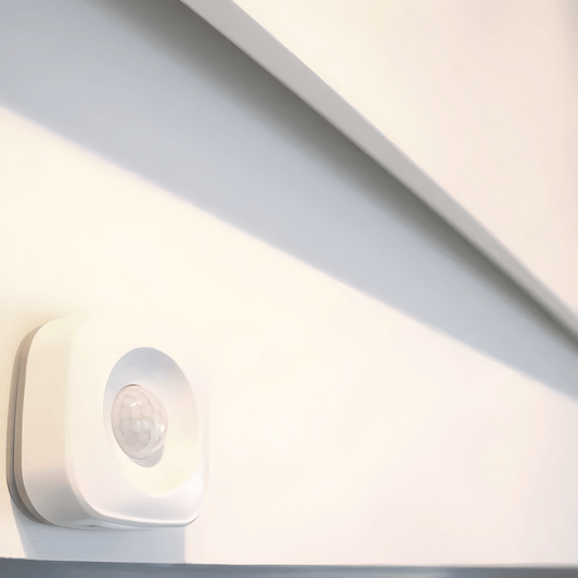 Witte PIR bewegingssensor gemonteerd op muur onder een wit infraroodpaneel